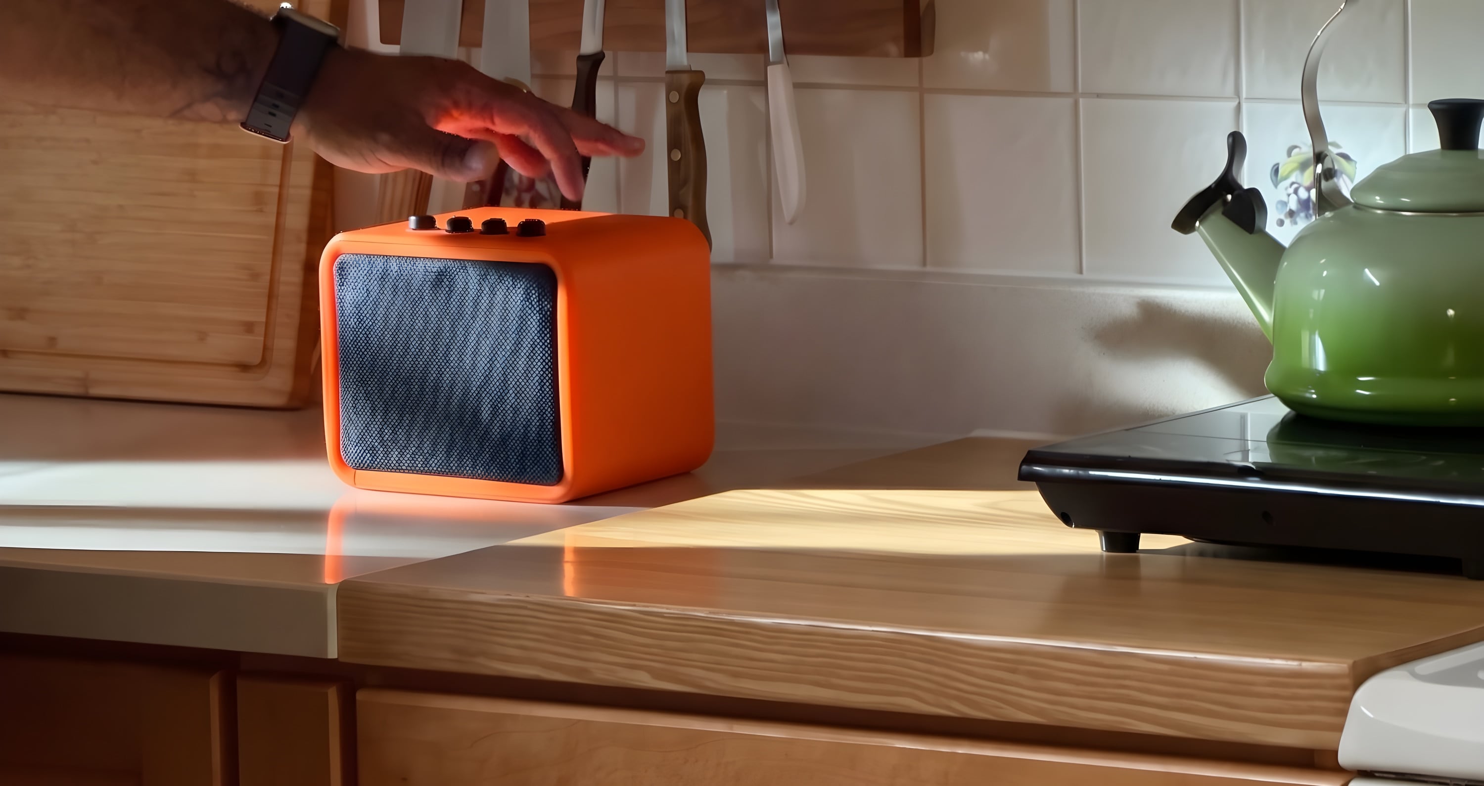 A hand pressing the top of an orange Shelter Radio on a kitchen counter